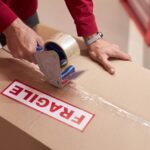 storage worker taping boxes in warehouse f6ajljv